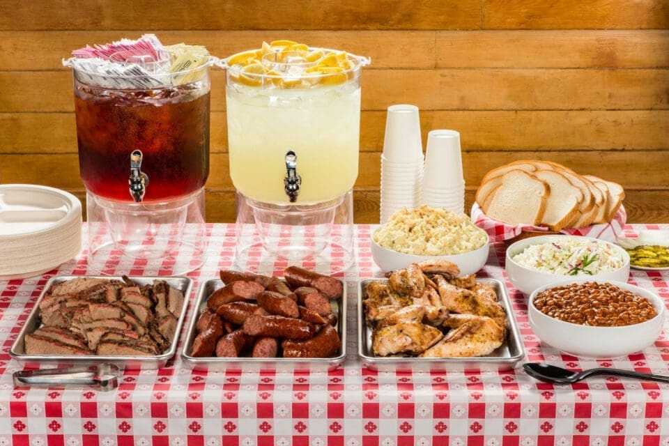 Lockhart Texas with kids — authentic Texas BBQ spread laid out on a picnic table with meats, sides, and cold drinks