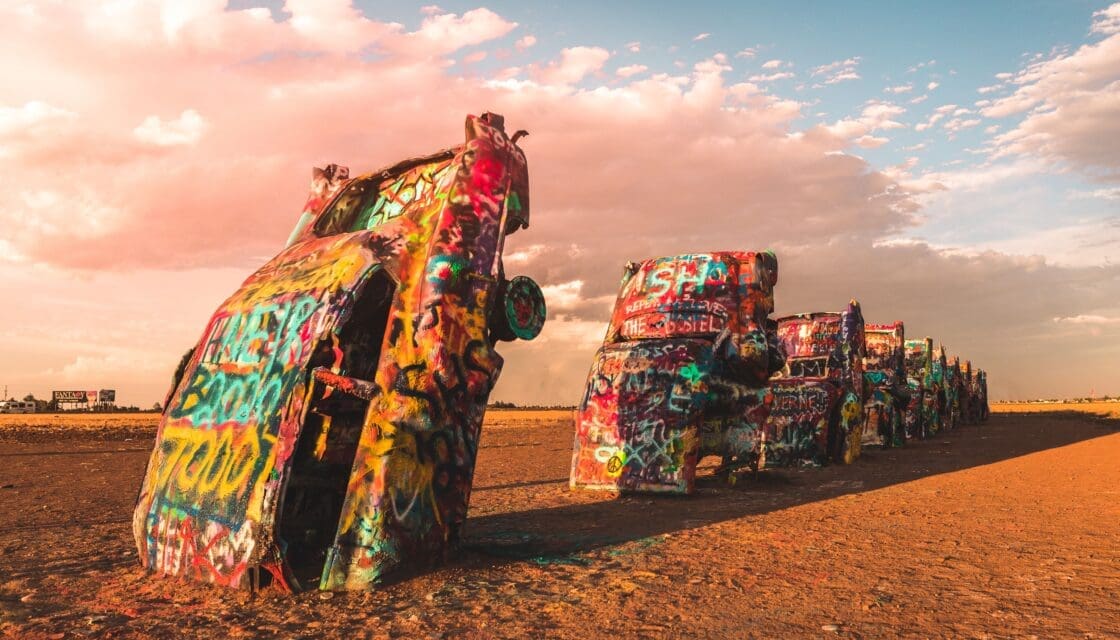 Sunset view at Cadillac Ranch in Amarillo, Texas, featuring the iconic graffiti-covered vintage Cadillac cars buried nose-first in the Texas panhandle landscape