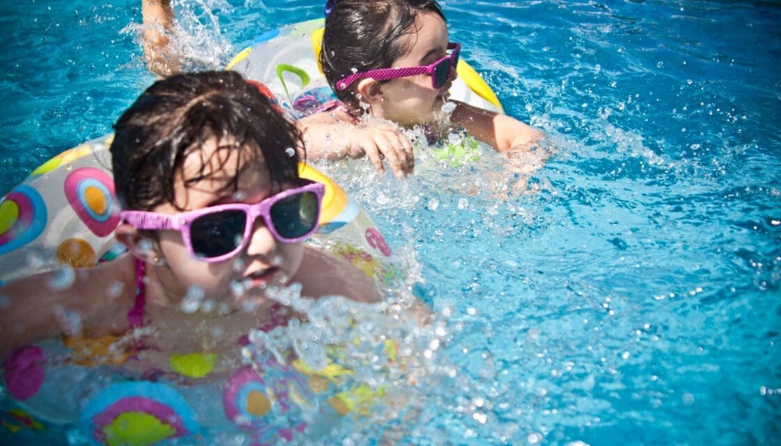 Barton Springs Pool with kids — two girls splashing and swimming in clear blue outdoor water on a sunny day