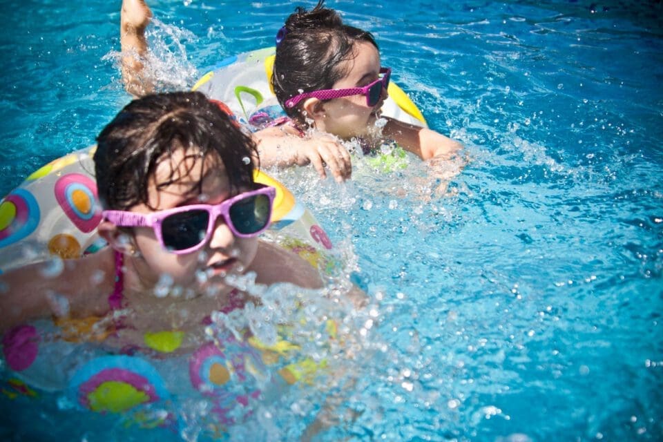 Barton Springs Pool with kids — two girls splashing and swimming in clear blue outdoor water on a sunny day
