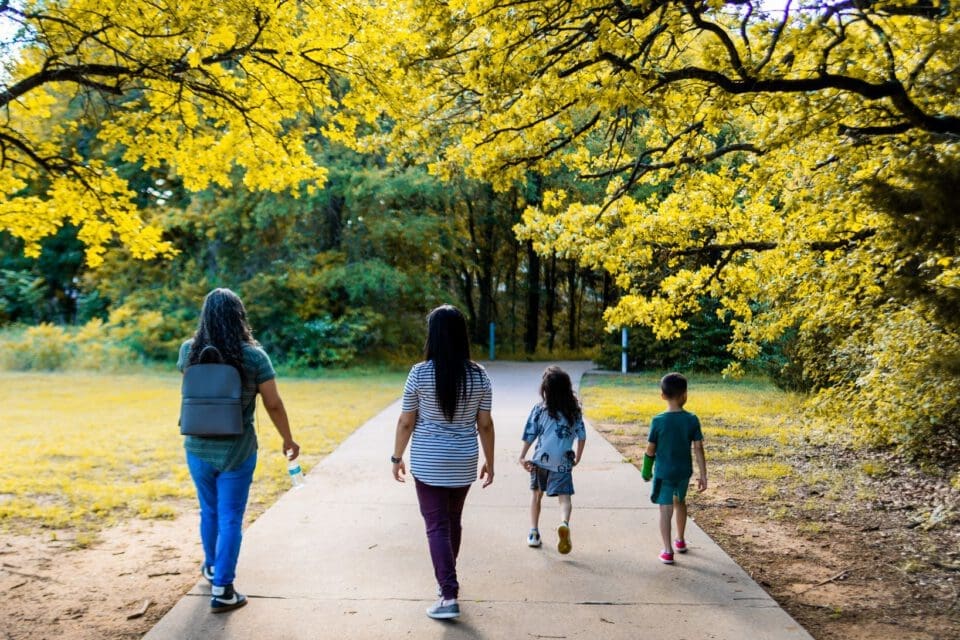 Brackenridge Park San Antonio stroller — women and children walking along a tree-lined park pathway in golden light