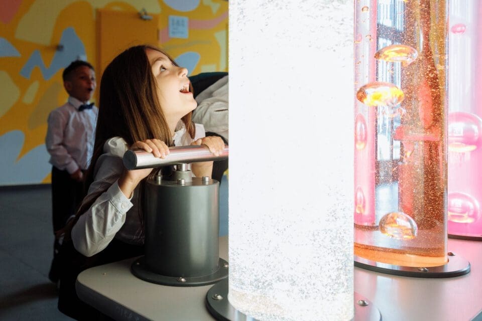 DoSeum San Antonio with kids — girl leaning in with fascination at colorful interactive science exhibit with glowing liquids